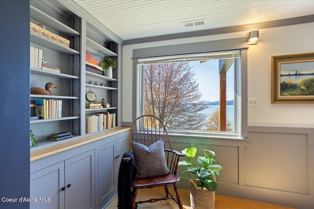 living area with built in features, crown molding, a wainscoted wall, and a decorative wall