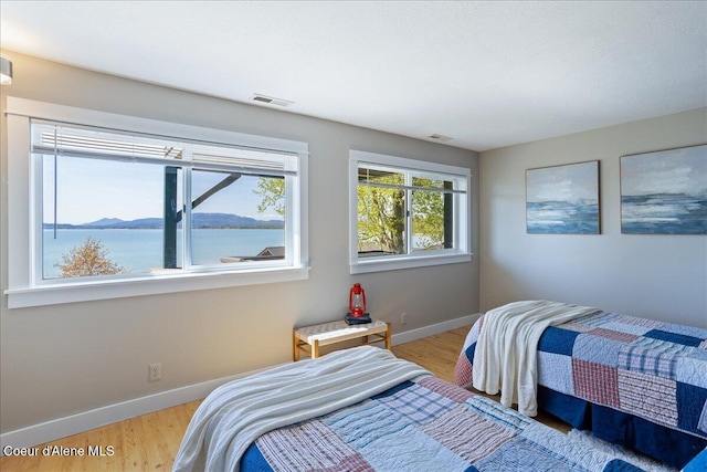 bedroom with baseboards, light wood-type flooring, and a water view
