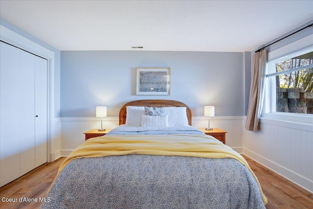 bedroom featuring wood finished floors, a wainscoted wall, and a closet