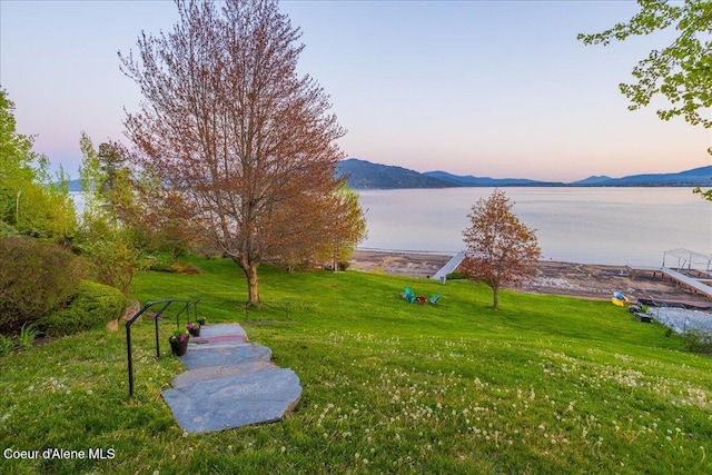 yard at dusk featuring a lawn and a water and mountain view