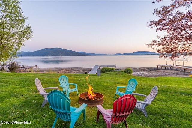 view of grassy yard with an outdoor fire pit and a water and mountain view