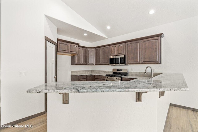 1451 W Tali Ave, Post Falls, ID 83854 - kitchen with appliances with stainless steel finishes, a peninsula, light stone counters, lofted ceiling, and light wood-type flooring