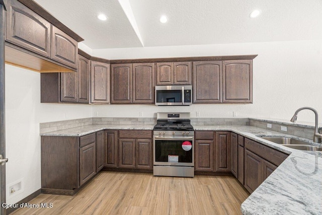 1451 W Tali Ave, Post Falls, ID 83854 - kitchen featuring stainless steel appliances, light wood-style floors, light stone countertops, dark brown cabinetry, and recessed lighting
