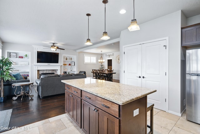1823 N Clark Fork Pkwy, Post Falls, ID 83854 - kitchen featuring freestanding refrigerator, a ceiling fan, a breakfast bar, a tiled fireplace, and hanging light fixtures