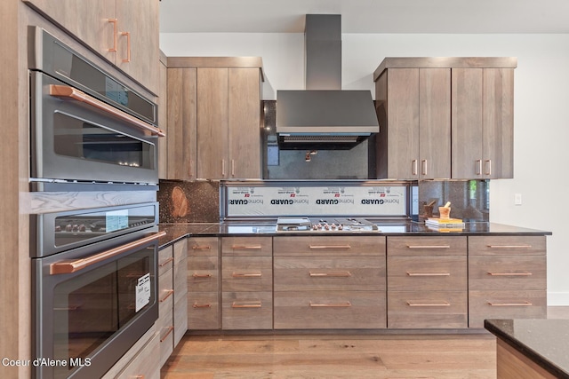2855 W Lumber Ln, Coeur Dalene, ID 83814 - kitchen featuring wall chimney exhaust hood, backsplash, dark stone counters, appliances with stainless steel finishes, and light wood-style floors