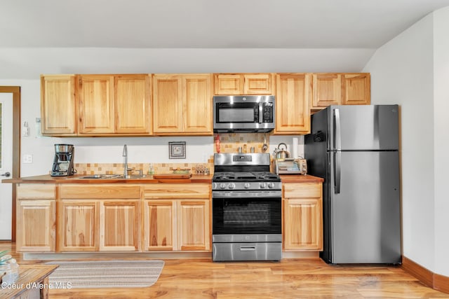 3226 District Two Rd, Bonners Ferry, ID 83805 - kitchen with stainless steel appliances, a sink, light brown cabinets, vaulted ceiling, and light wood-style flooring