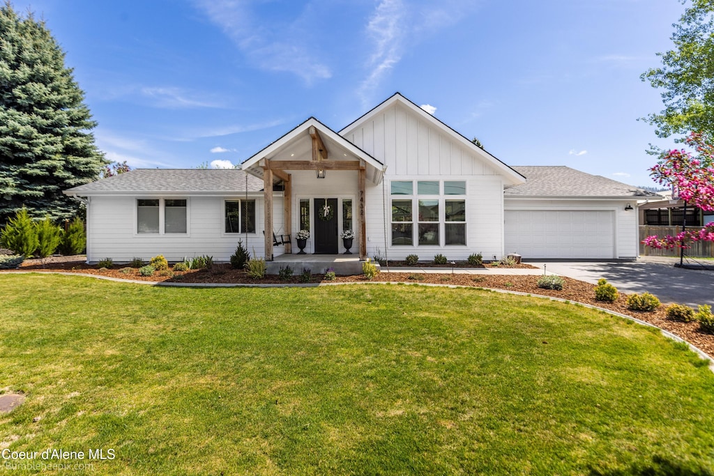 view of front of property featuring board and batten siding, an attached garage, a front yard, driveway, and a shingled roof