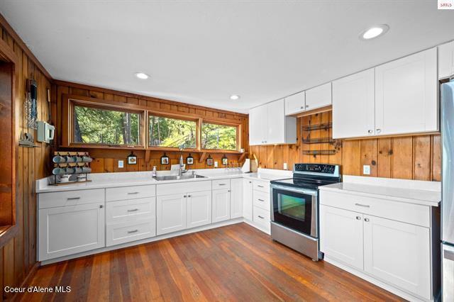 24010 N Bridge Lake Rd, Rathdrum, ID 83858 - kitchen featuring appliances with stainless steel finishes, a sink, wood walls, light countertops, and dark wood-style flooring