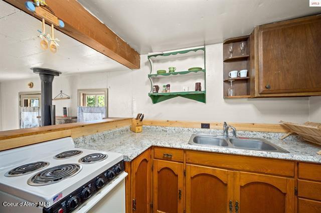 24010 N Bridge Lake Rd, Rathdrum, ID 83858 - kitchen with white range with electric cooktop, a sink, brown cabinetry, open shelves, and light stone counters
