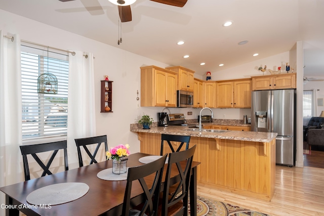 kitchen with appliances with stainless steel finishes, ceiling fan, a peninsula, a sink, and light wood-type flooring