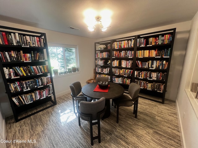 sitting room with wall of books, wood finished floors, baseboards, and a chandelier