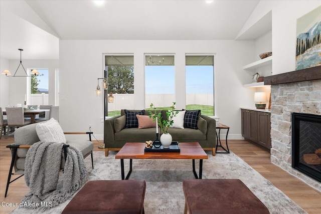 living area featuring lofted ceiling, light wood-style flooring, a fireplace, a chandelier, and baseboards