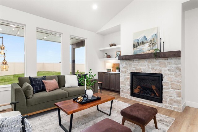 living room featuring light wood-type flooring, a stone fireplace, built in features, and lofted ceiling