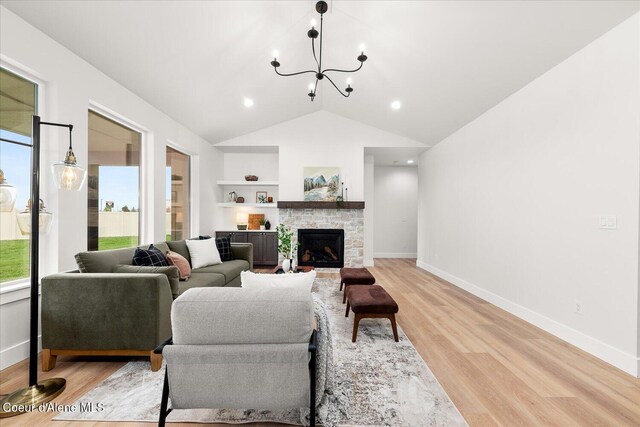 living room with lofted ceiling, a stone fireplace, light wood-style floors, built in shelves, and a chandelier