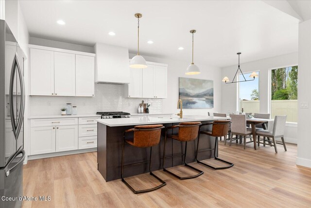 kitchen with stainless steel fridge, custom range hood, light countertops, light wood finished floors, and backsplash