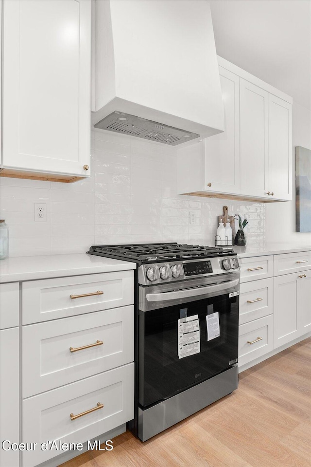 kitchen featuring stainless steel gas range, custom exhaust hood, white cabinetry, light countertops, and decorative backsplash