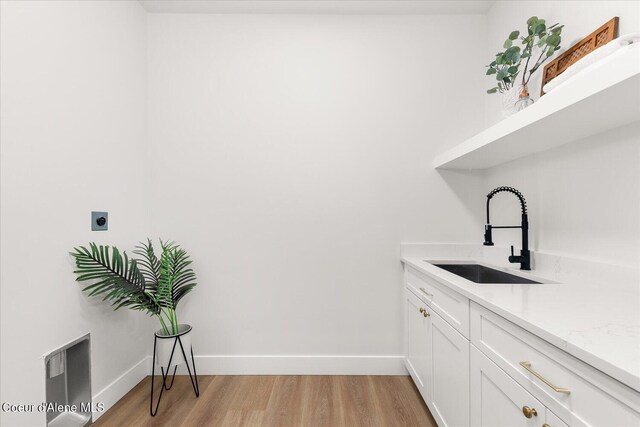 clothes washing area with electric dryer hookup, cabinet space, light wood-style floors, and baseboards