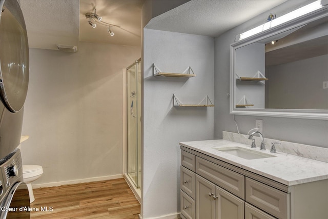4413 W Pleasant Ln, Post Falls, ID 83854 - full bathroom featuring stacked washer and clothes dryer, wood finished floors, a stall shower, toilet, and a textured ceiling