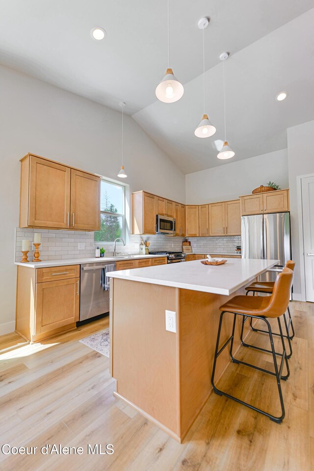 204 Silver Saddle Ct, Pinehurst, ID 83850 - kitchen with stainless steel appliances, light wood-style flooring, vaulted ceiling, a kitchen island, and backsplash