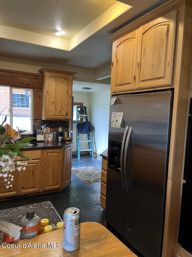 kitchen with stainless steel fridge, stone tile floors, a raised ceiling, tasteful backsplash, and dark countertops