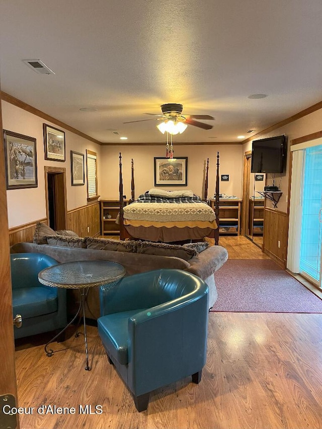bedroom with a wainscoted wall, crown molding, wood finished floors, wood walls, and a ceiling fan