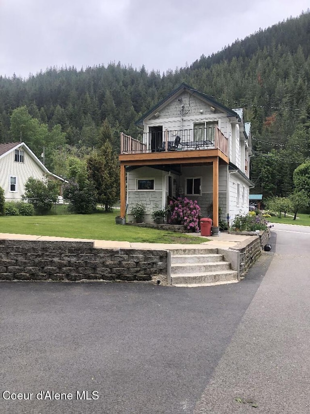 view of front facade featuring a forest view, a front lawn, and a deck