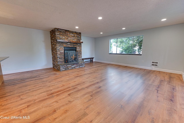 unfurnished living room with a textured ceiling, wood finished floors, a stone fireplace, recessed lighting, and baseboards