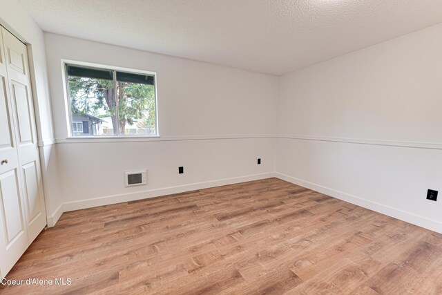 empty room featuring light wood-style flooring, baseboards, and a textured ceiling