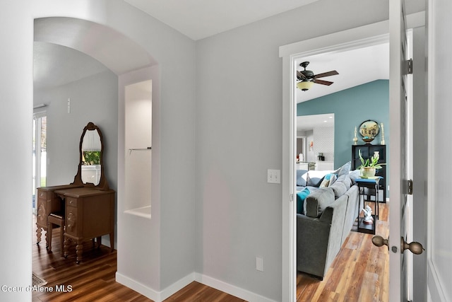 corridor with light wood-style floors, lofted ceiling, arched walkways, and baseboards
