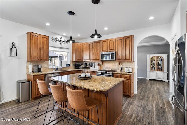 8747 Salmonberry Lp, Hayden, ID 83835 - kitchen with stainless steel appliances, a center island, arched walkways, brown cabinetry, and light stone counters