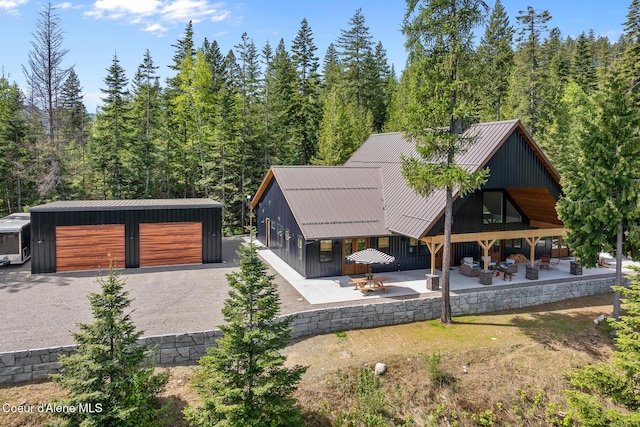 rear view of house featuring a patio, a garage, a wooded view, and metal roof