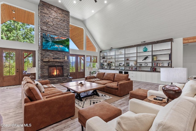living area with light wood finished floors, high vaulted ceiling, healthy amount of natural light, a stone fireplace, and recessed lighting