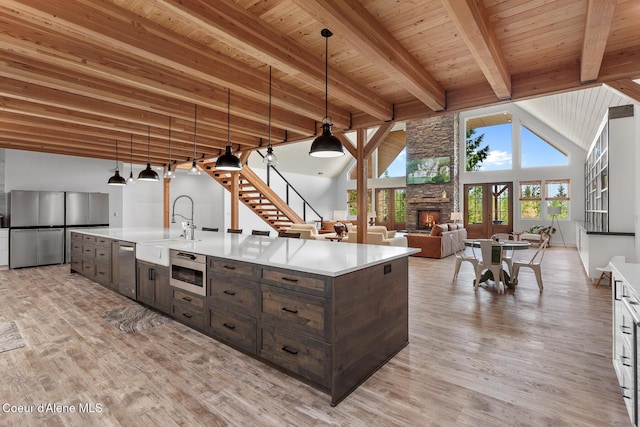 kitchen with appliances with stainless steel finishes, dark brown cabinets, light countertops, light wood-type flooring, and beamed ceiling