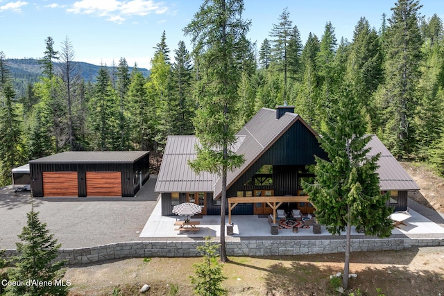 view of front of house featuring a forest view, metal roof, an outbuilding, a standing seam roof, and a patio area