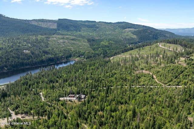 drone / aerial view of a heavily wooded area and a water and mountain view