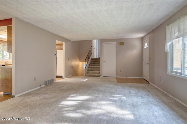unfurnished living room with healthy amount of natural light, stairway, carpet, baseboards, and a textured ceiling