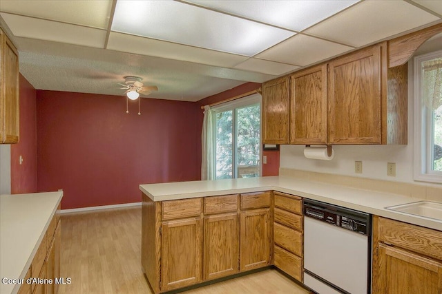 kitchen featuring white dishwasher, a peninsula, a ceiling fan, light wood-style floors, and plenty of natural light