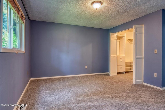 unfurnished bedroom featuring carpet, a textured ceiling, baseboards, and a spacious closet