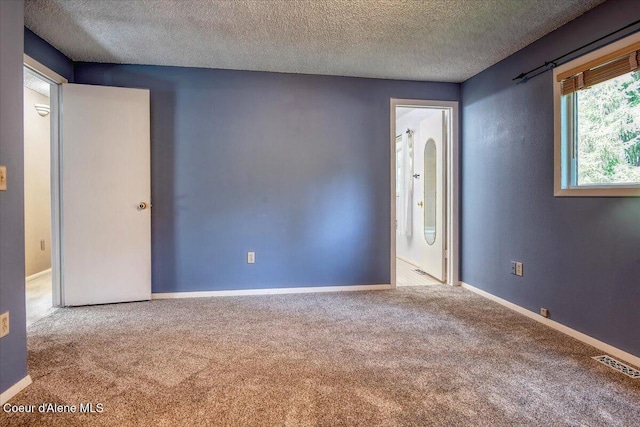 carpeted spare room featuring a textured ceiling and baseboards