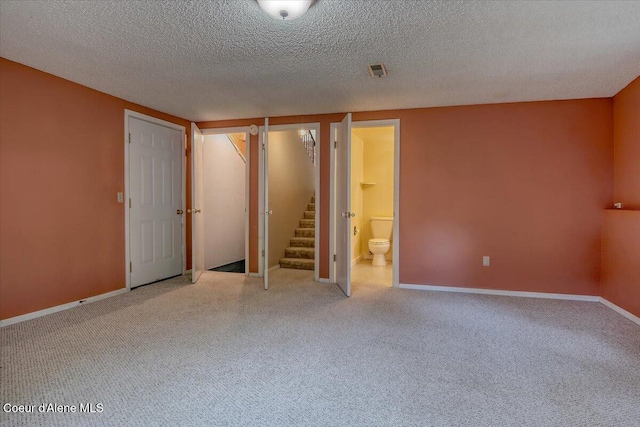 unfurnished room featuring carpet floors, stairway, baseboards, and a textured ceiling