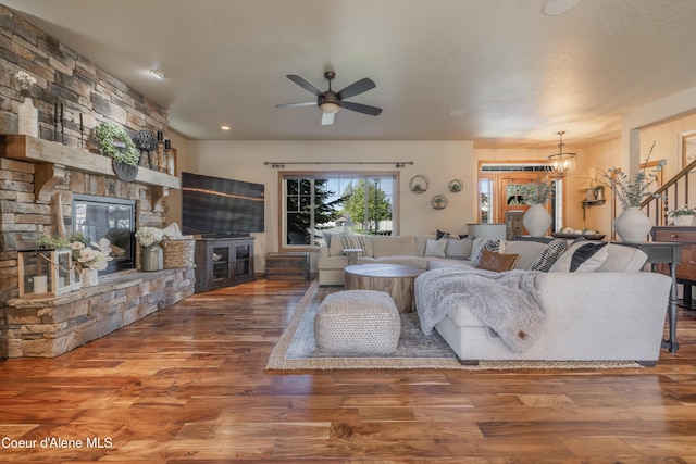 living room with a ceiling fan, a stone fireplace, wood finished floors, and a chandelier