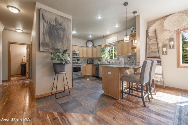 kitchen with stainless steel appliances, light brown cabinetry, a peninsula, a breakfast bar, and baseboards