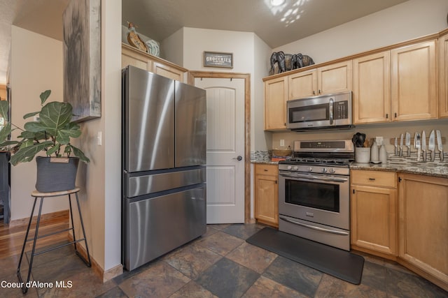 kitchen with stainless steel appliances, light brown cabinetry, light stone countertops, baseboards, and dark stone finish floors