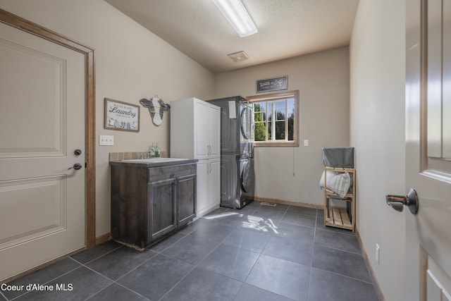 washroom featuring cabinet space, estacked washer and dryer, baseboards, and dark tile patterned floors