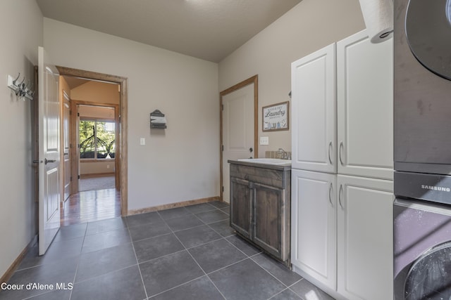 bathroom featuring baseboards, tile patterned flooring, stacked washer and clothes dryer, and vanity