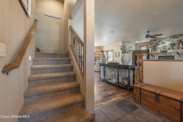 stairway featuring ceiling fan, a stone fireplace, and wood finished floors