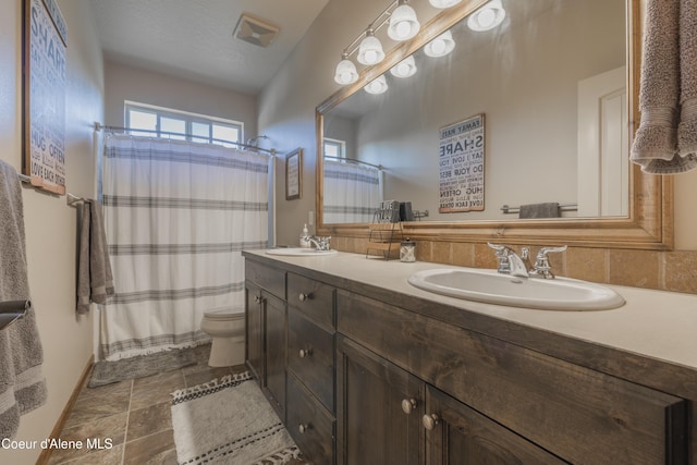 full bath with toilet, double vanity, a shower with shower curtain, and stone finish flooring