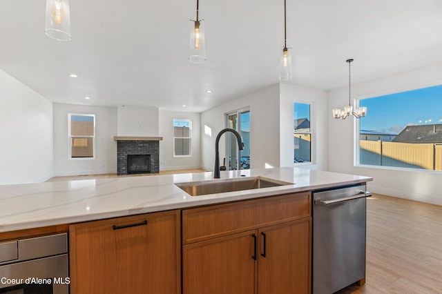 kitchen featuring stainless steel dishwasher, a sink, a fireplace, open floor plan, and hanging light fixtures