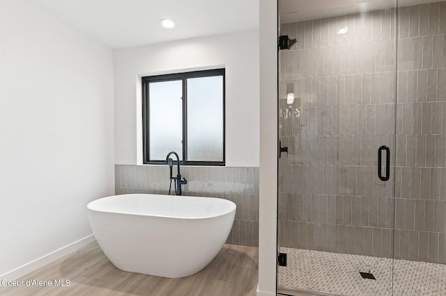 bathroom with wood finished floors, a shower stall, a freestanding bath, tile walls, and recessed lighting