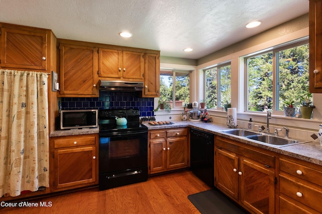 249 Gun Club Rd, Sagle, ID 83860 - kitchen featuring black appliances, a sink, under cabinet range hood, brown cabinets, and light wood-style floors